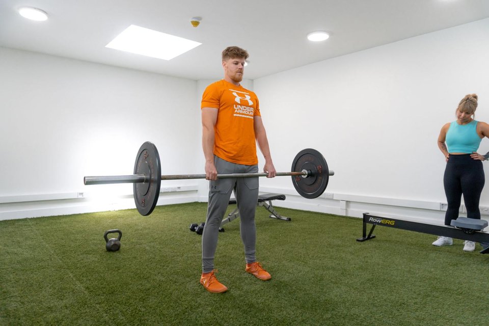Victor with a barbell in the turf studio, a client training behind him