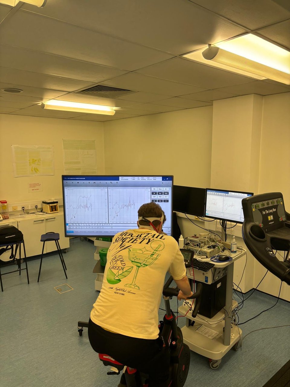 Rider on a lab bike during performance testing, monitors showing live data